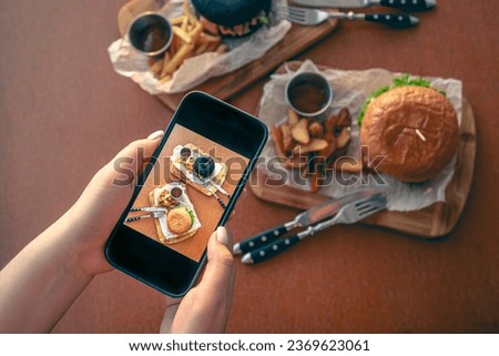 A woman takes pictures of burgers on her smartphone.