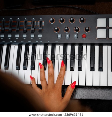 Woman with red nails playing electronic musical keyboard synthesizer.