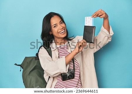 Filipina traveler displaying flight ticket with camera and backpack on blue Royalty-Free Stock Photo #2369644611
