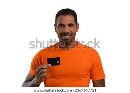 A man with a black credit card in his hand, wearing a basic orange T-shirt, looks at the camera and smiles, white background