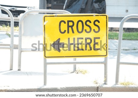 cross here with arrow writing caption text street road sign on island in middle of road in black on yellow
