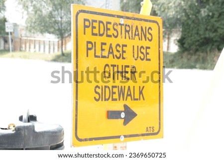 pedestrians please use other sidewalk writing caption text sign with arrow pointing right east orange and black on bright summer day