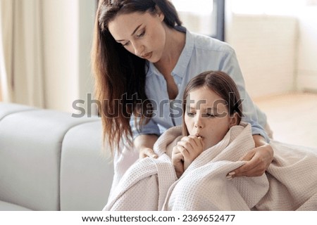 Sick kid catching cold, coughing, staying at home. Caring mother covering child with soft blanket. Daughter sitting on sofa, have first symptoms of flu virus Royalty-Free Stock Photo #2369652477