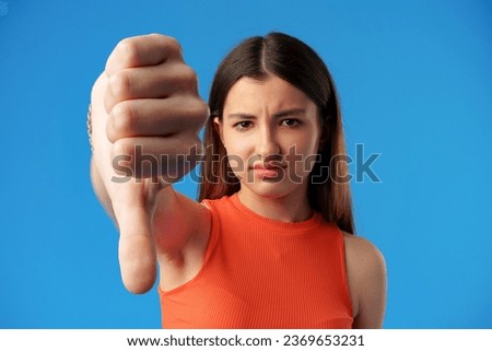 Teen girl over blue background showing thumbs down gesture