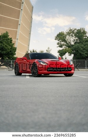 A striking red American sports car, the epitome of speed and style, standing alone in an expansive empty car park. Royalty-Free Stock Photo #2369655285