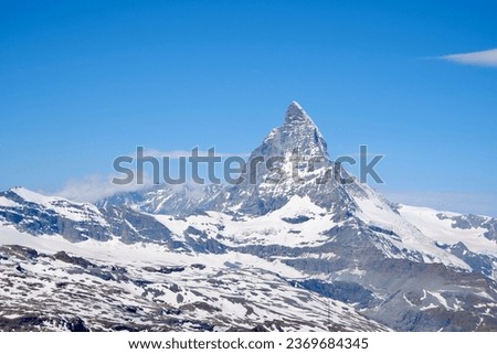 A photo of Matterhorn covered in snow against a clear blue sky. The snow on the mountain is white and pristine, and the sky is a brilliant blue. There are a few clouds in the sky.