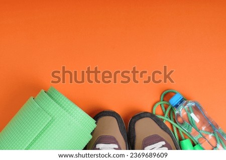 Realistic fitness elements. Fitness and workout concept with copy space. sneakers, bottle of water, green yoga mat and jump rope on an orange background