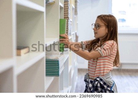 Long-haired girl in eyeglasses putting a book on the shelf Royalty-Free Stock Photo #2369690985
