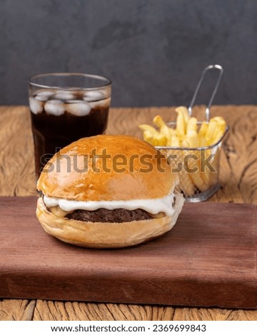 Cheeseburger with mayonnaise over wooden board with french fries and soda.