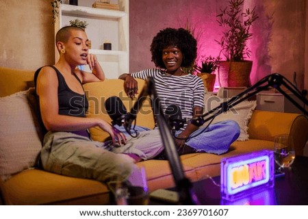 Happy diverse female podcasters having a interesting conversation in a home studio while recording an internet podcast for their social media channel. Focus on an african woman with afro hair.