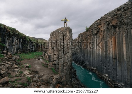 An explorer is standing on a cliff next to the canyon in the wild nature of Iceland and feeling free. A discoverer is exploring wildness and canyon in nature in Iceland.