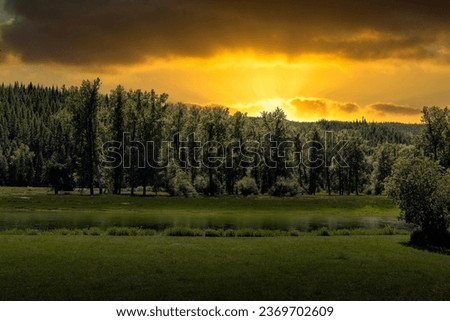 A INTENSE SUNSET WITH A CLOUDY SKY AND NUMEROUS EVERGEEN TREES WITH A BEAUTIFUL RIVER IN IDAHO