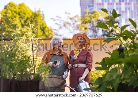 Portrait of senior friends taking care of vegetable plants in urban garden.