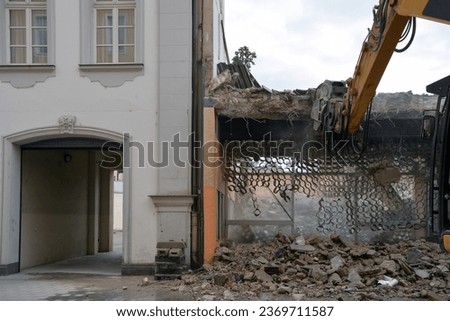 Dismantling part of the house with an excavator with a manipulator. The transport entrance from the side of the arch is intact. Royalty-Free Stock Photo #2369711587