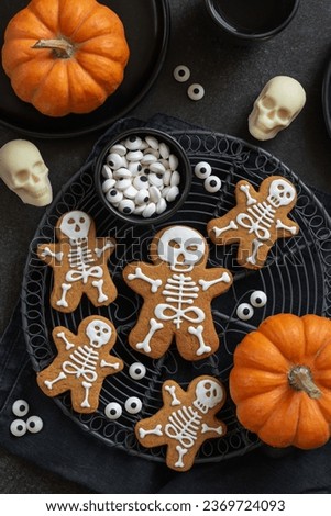 Homemade Halloween treats for kids. Funny skeleton gingerbread men icing cookies, white chocolate sculls and candy eyes. Black background, top view