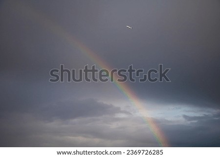 Rainbow and airplane on stormy dark sky background. Nature and technology concept. Travel and adventures. The plane gains altitude during takeoff