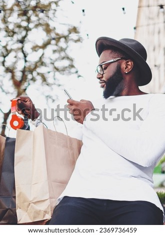 Dark skinned man checking purchases holding mobile phone 
