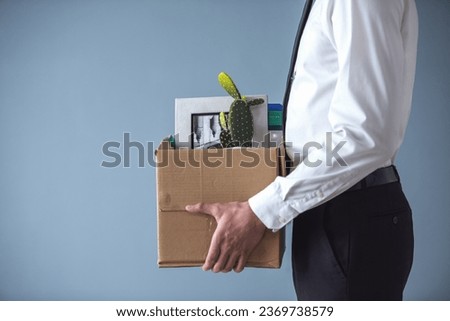 Getting fired. Cropped image of handsome businessman in formal wear holding a box with his stuff, on gray background Royalty-Free Stock Photo #2369738579