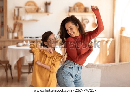 Funny Family Leisure. Cheerful european mother and daughter moving and dancing to music enjoying time together, having party fun on weekend and fooling at modern home interior in living room Royalty-Free Stock Photo #2369747257