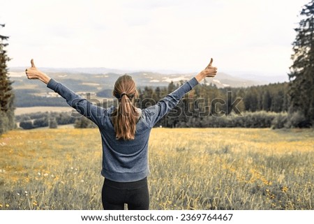 Young woman walking in a meadow with thumbs up enjoying peace serenity in nature  Royalty-Free Stock Photo #2369764467