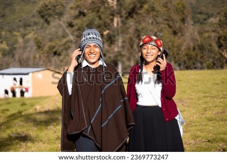 Quechua native man wearing a chullo, poncho and phone next to an attractive woman holding cell phone in her hand, outdoors, communication Royalty-Free Stock Photo #2369773247