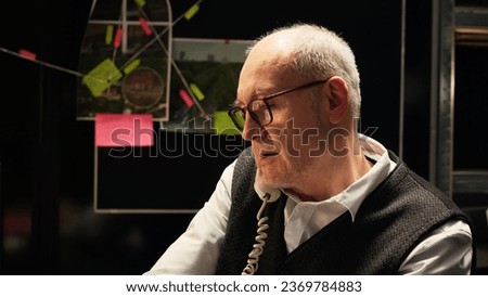 Law agent finding new case clues, receiving classified information on landline phone call. Experienced investigator writing intelligence on files, detecting lawbreaker. Handheld shot. Royalty-Free Stock Photo #2369784883