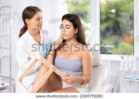 Young brunette female patient sitting in front of mirror at beauty center room consulting by female aesthetician Royalty-Free Stock Photo #2369790281
