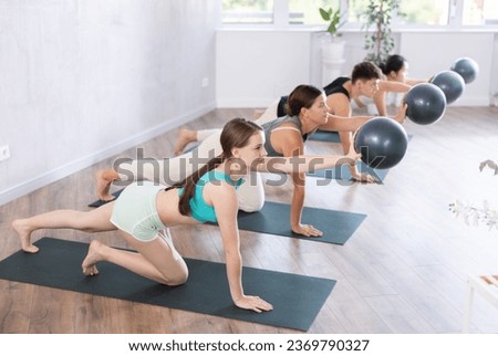 Group of relaxed young people in 20s in sportswear sitting on mats doing pilates holding mini ball in hands in gym in morning. Royalty-Free Stock Photo #2369790327