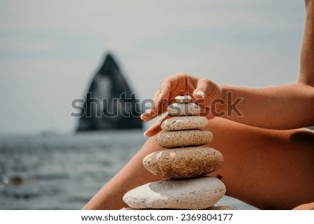 Woman building a stone pyramid on the seashore on a sunny day. Blue sea background. Travel destination, relaxation and meditation concept.