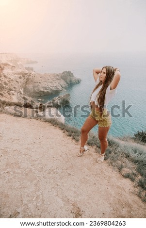 Woman travel sea. Happy tourist enjoy taking picture outdoors for memories. Woman traveler looks at the edge of the cliff on the sea bay of mountains, sharing travel adventure journey