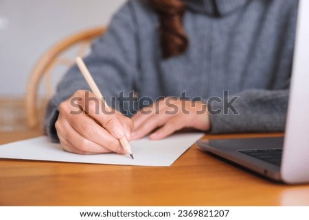Closeup image of a young woman writing on paper while working on laptop computer at home