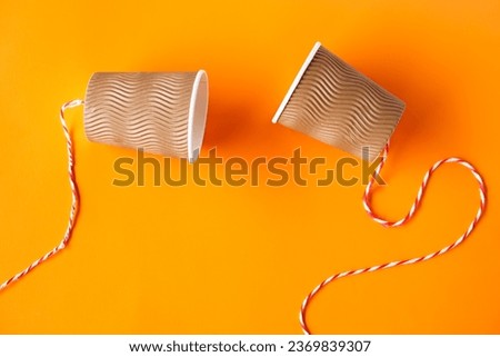 DIY paper cups with string on orange background. Concept, telephone toys which apply with science knowledge about vibration sound through straining strings causing us to hear the sound.               