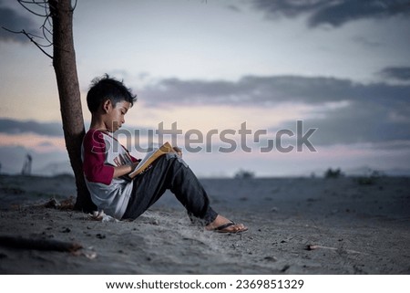 Little boy with the book study hard on the beach at sunset                               