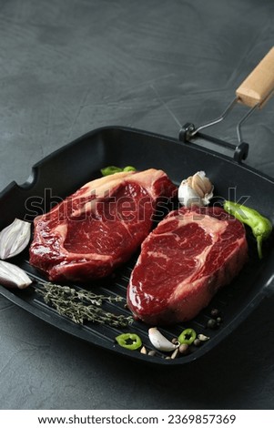 Grill pan with pieces of fresh beef meat, thyme and spices on gray table, space for text