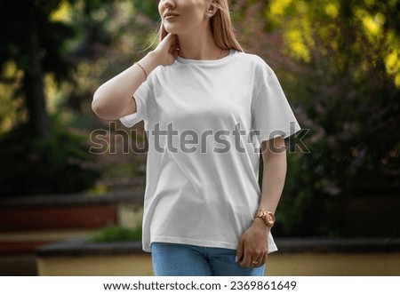 Mockup of a white stylish t-shirt on a posing girl on a blurred background of a green park, front view. Streetwear template for presentation of design, pattern. Shirt for a woman. Product photography