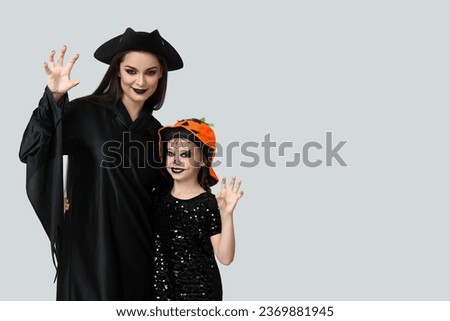 Little girl with her mother dressed for Halloween on light background