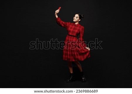 Full body young woman with Halloween makeup face art mask wear clown costume red dress do selfie shot on mobile cell phone isolated on plain solid black background studio. Scary holiday party concept