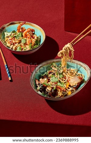 Vibrant Asian wok noodles set against a striking red backdrop, accompanied by chopsticks. Minimalistic design capturing the essence of bold, flavorful cuisine. Royalty-Free Stock Photo #2369888995