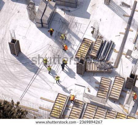 Workers in orange and yellow uniform working with reinforcement at the construction site, gray concrete background. Daylight, top view. High quality photo