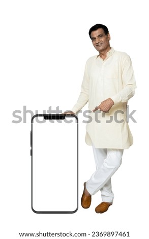 Mock-up Indian Senior man in ethnic wear showing smartphone with empty screen, points finger at blank device display isolated on black, male advertising new mobile app