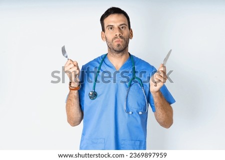 hungry young doctor man wearing medical uniform holding in hand fork knife want tasty yummy pizza pie Royalty-Free Stock Photo #2369897959