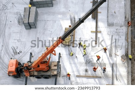 Workers in orange and yellow uniform working with reinforcement and rebars at the construction site, gray concrete background. Stack of bars and box around. High quality photo