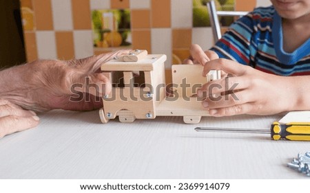 A five-year-old boy independently assembles a wooden construction kit with a screwdriver. Hands close-up