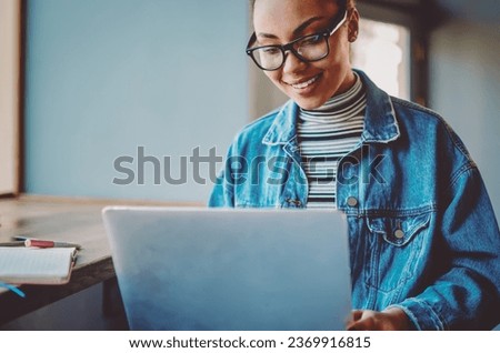 Positive dark skinned female student enjoying time for online shopping during leisure time for herself