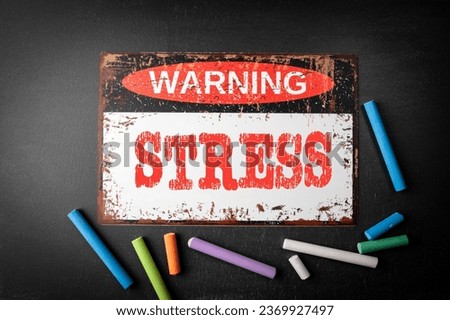 Stress Concept. Metal warning sign and colored pieces of chalk on a dark chalkboard background.