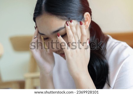 Side view portrait of beautiful young Asian girl sitting on floor and touching her temples feeling stress. Selective on hand.