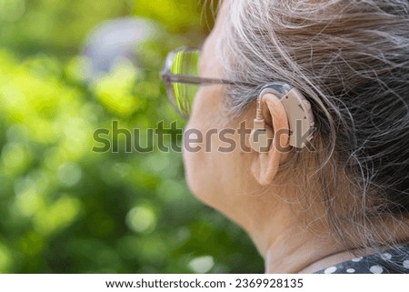 Middle age woman wearing eyeglasses and using hearing aid while sitting on chair in the garden at home. The problem of hearing in old age concept.