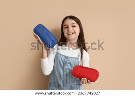 Little girl with pencil cases on beige background Royalty-Free Stock Photo #2369942027