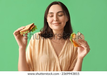 Beautiful young woman with tasty sandwiches on green background Royalty-Free Stock Photo #2369943815