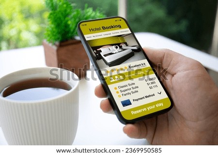 Man hand hold phone with hotel booking application background of table in cafe